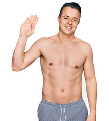 Fototapeta premium Handsome young man wearing swimwear shirtless waiving saying hello happy and smiling, friendly welcome gesture