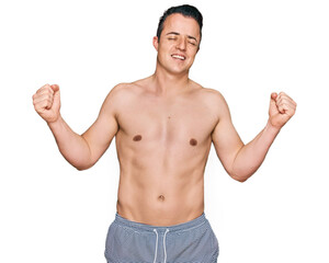 Fototapeta premium Handsome young man wearing swimwear shirtless very happy and excited doing winner gesture with arms raised, smiling and screaming for success. celebration concept.