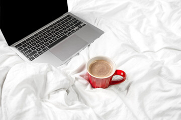 Red cup with coffee and laptop on the bed in the bedroom