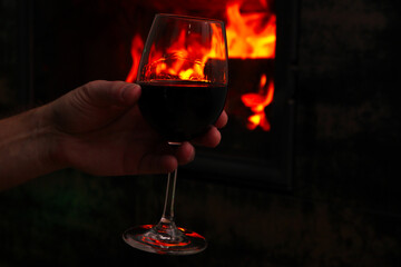 Mans hand holds the wine glass in front of the fireplace. Blur burning fireplace background.