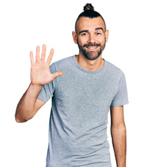 Hispanic man with ponytail wearing casual grey t shirt showing and pointing up with fingers number five while smiling confident and happy.