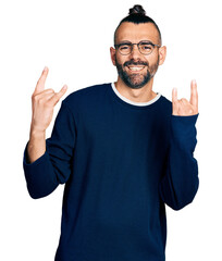 Hispanic man with ponytail wearing casual sweater and glasses shouting with crazy expression doing...