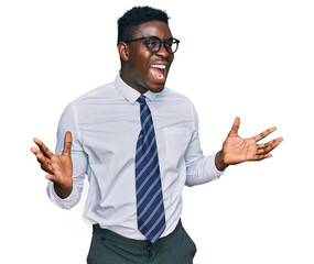 Handsome business black man wearing white shirt and tie celebrating mad and crazy for success with arms raised and closed eyes screaming excited. winner concept