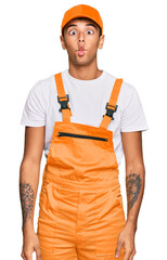 Young handsome african american man wearing handyman uniform making fish face with lips, crazy and comical gesture. funny expression.