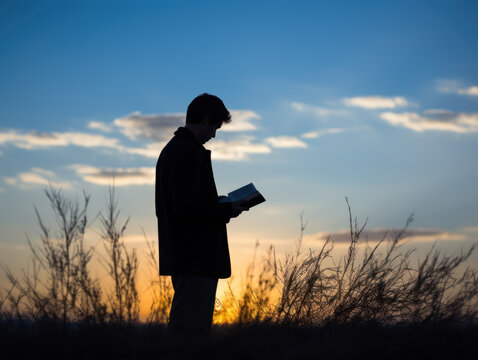 silhouette of man reading a book about scriptures in a field at sunset