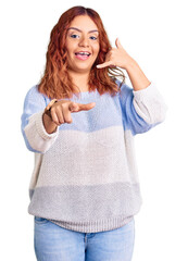 Young latin woman wearing casual clothes smiling doing talking on the telephone gesture and...
