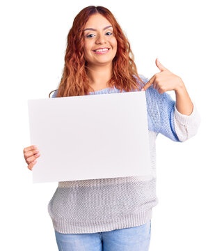 Young latin woman holding blank empty banner pointing finger to one self smiling happy and proud