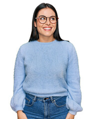Young hispanic woman wearing casual clothes and glasses looking away to side with smile on face,...