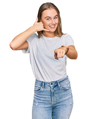 Beautiful young blonde woman wearing casual white t shirt smiling doing talking on the telephone gesture and pointing to you. call me.