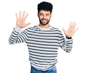 Naklejka premium Young arab man with beard wearing casual striped sweater showing and pointing up with fingers number ten while smiling confident and happy.