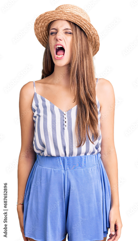 Wall mural Young beautiful blonde woman wearing summer hat angry and mad screaming frustrated and furious, shouting with anger. rage and aggressive concept.