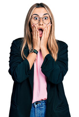 Hispanic young woman wearing business jacket and glasses afraid and shocked, surprise and amazed...