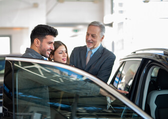 Young family talking to the salesman and choosing their new car in a showroom