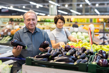 Mature buyer man chooses ripe eggplant on grocery store window