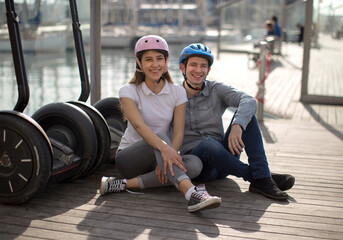 Young couple guy and girl are walking on the segway along the board paved promenade in the port of...