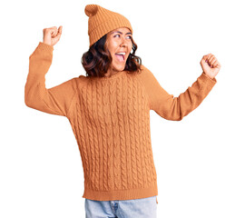Naklejka premium Young beautiful mixed race woman wearing wool sweater and winter hat dancing happy and cheerful, smiling moving casual and confident listening to music