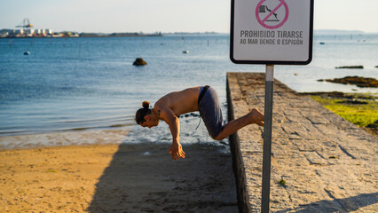 guy jumping with a no diving sign on jetty on beach
