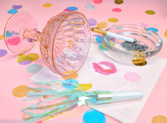 A Tipped of Champagne Glass, Party Horns, A Lipstick Stained Napkin, Confetti and a Cigarette in an...