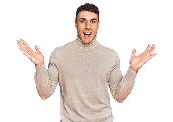 Fototapeta premium Hispanic young man wearing casual turtleneck sweater celebrating victory with happy smile and winner expression with raised hands