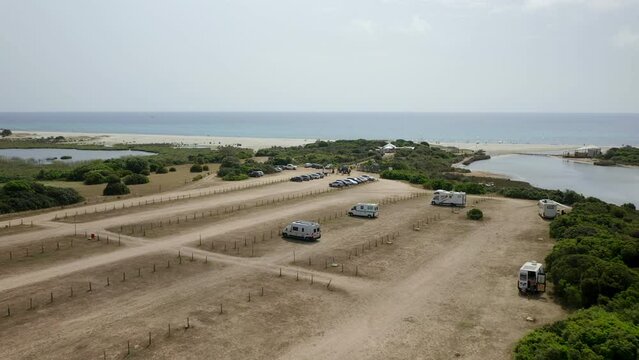 Aerial drone view of camper vans parked in wild Spiaggia di Berchida beach parking in Sardinia, Italy