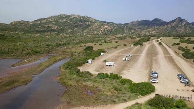 Aerial drone view of camper vans parked in wild Spiaggia di Berchida beach parking with mountain landscape in Sardinia, Italy