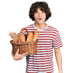 Caucasian teenager holding wicker basket with bread scared and amazed with open mouth for surprise, disbelief face