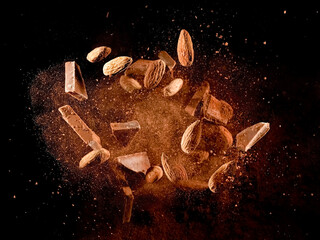 Chocolate pieces and almonds flying in dry cocoa powder explosion on black background