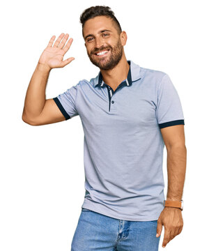 Handsome man with beard wearing casual clothes waiving saying hello happy and smiling, friendly welcome gesture