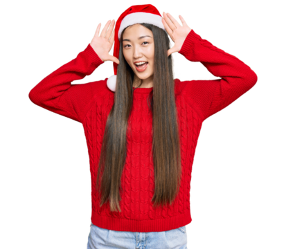 Young chinese woman wearing christmas hat smiling cheerful playing peek a boo with hands showing face. surprised and exited - Powered by Adobe