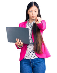 Naklejka premium Young beautiful chinese woman using laptop pointing with finger to the camera and to you, confident gesture looking serious