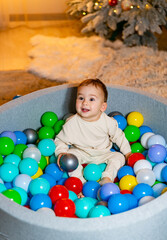 Fototapeta na wymiar A Joyful Baby Surrounded by Colorful Balls, Gazing at a Festive Christmas Tree. A baby sitting in a ball pit with a christmas tree in the background