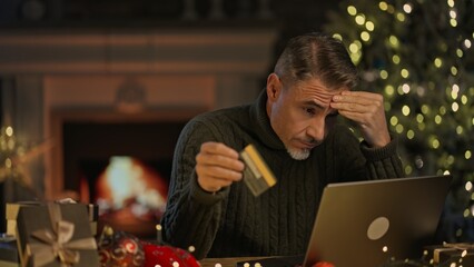Man sitting at laptop computer at home, paying with bank card, having problem in buying Christmas...