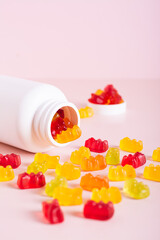 Chewable vitamin supplements spilled from a bottle on a pink background vertical view