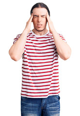 Young adult man with long hair wearing casual striped tshirt suffering from headache desperate and stressed because pain and migraine. hands on head.