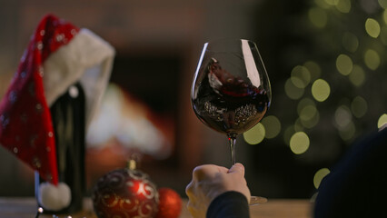 Glass and bottle of red wine on table in Christmas decorated home. Man swirling tasting buying...