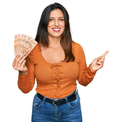Beautiful hispanic woman holding 50 brazilian real banknotes smiling happy pointing with hand and...
