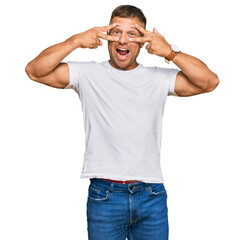 Handsome muscle man wearing casual white tshirt doing peace symbol with fingers over face, smiling cheerful showing victory