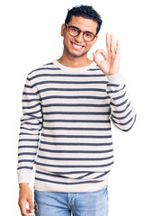 Fototapeta premium Hispanic handsome young man wearing casual clothes and glasses smiling positive doing ok sign with hand and fingers. successful expression.