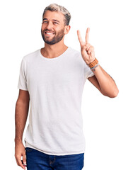 Young handsome blond man wearing casual t-shirt showing and pointing up with fingers number two while smiling confident and happy.
