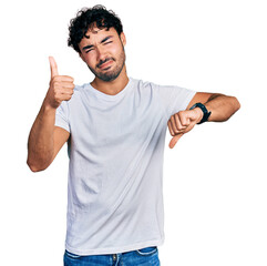 Hispanic young man with beard wearing casual white t shirt doing thumbs up and down, disagreement and agreement expression. crazy conflict
