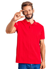 Handsome blond man with beard wearing casual clothes smiling and confident gesturing with hand doing small size sign with fingers looking and the camera. measure concept.