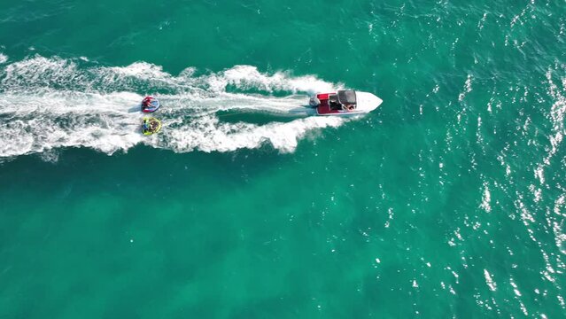 Aerial drone video of extreme inflatable towable tube cruising in high speed attached on powerboat with children riding, watersport