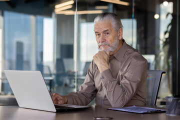 Portrait of an older gray-haired businessman sitting in the office at the table, working on a...
