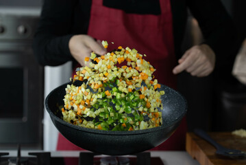 Chef cook roasts vegetables in wok pan on gas stove. Flying vegetable food levitation in motion, skillfully tossed by the chef hand. Airborne creative culinary expertise.