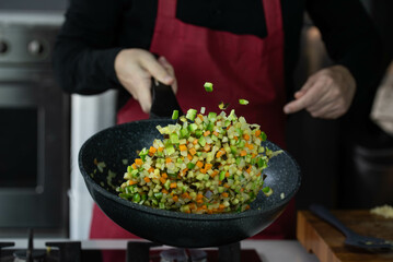 Chef cook roasts vegetables in wok pan on gas stove. Flying vegetable food levitation in motion, skillfully tossed by the chef hand. Airborne creative culinary expertise.