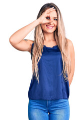 Young beautiful blonde woman wearing casual sleeveless t-shirt smiling happy doing ok sign with hand on eye looking through fingers