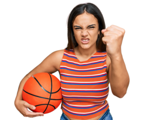 Young brunette woman holding basketball ball annoyed and frustrated shouting with anger, yelling crazy with anger and hand raised