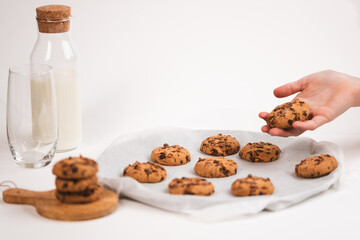 Hands take fresh cookies from plate, close-up,Close-up of hand grabbing a freshly baked cookie on white background with milk bottle and glass