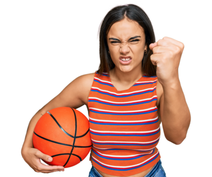 Young brunette woman holding basketball ball annoyed and frustrated shouting with anger, yelling crazy with anger and hand raised