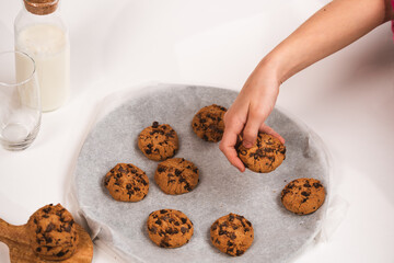 Hands take fresh cookies from plate, close-up,Close-up of hand grabbing a freshly baked cookie on white background with milk bottle and glass